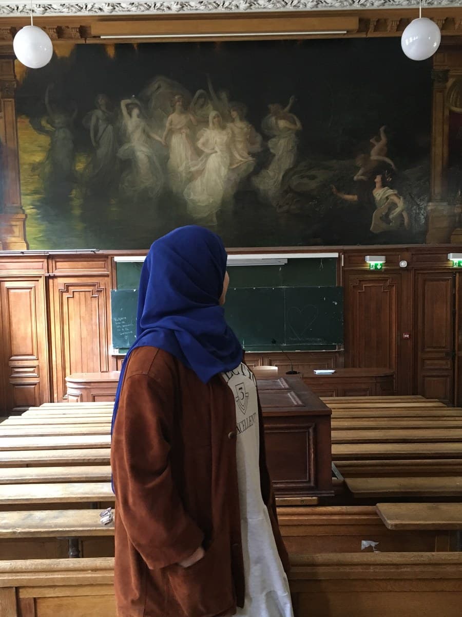 Yasmine Barkaoui looking up at the painting in a Sorbonne lecture hall