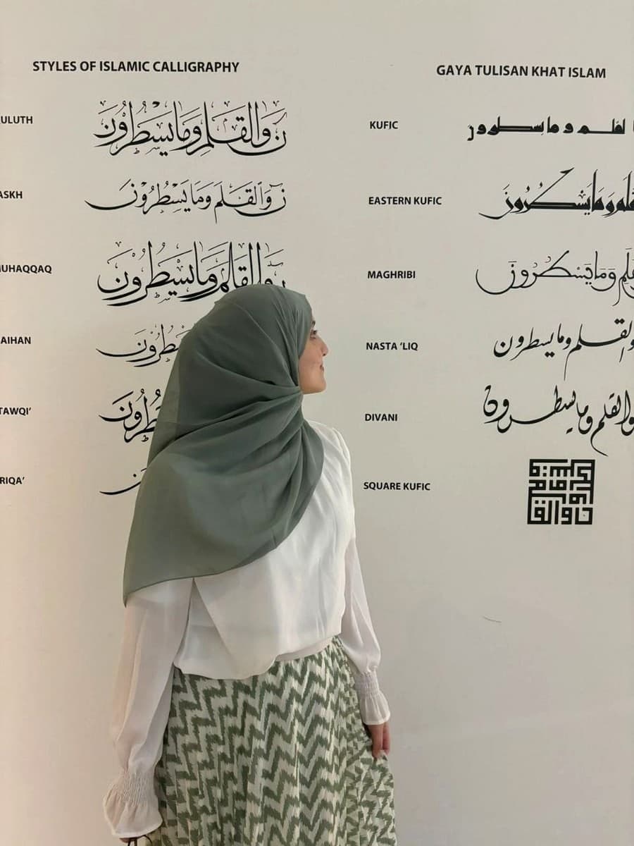 Yasmine Barkaoui in front of a wall of Arabic calligraphy styles in a museum